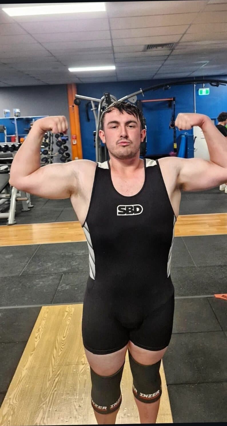 Loki after, flexing in a powerlifting singlet