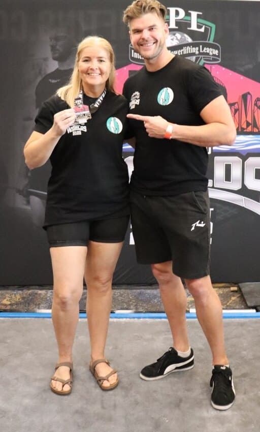 Michelle holding up her medal from the powerlifting Worlds, with Chris beside her